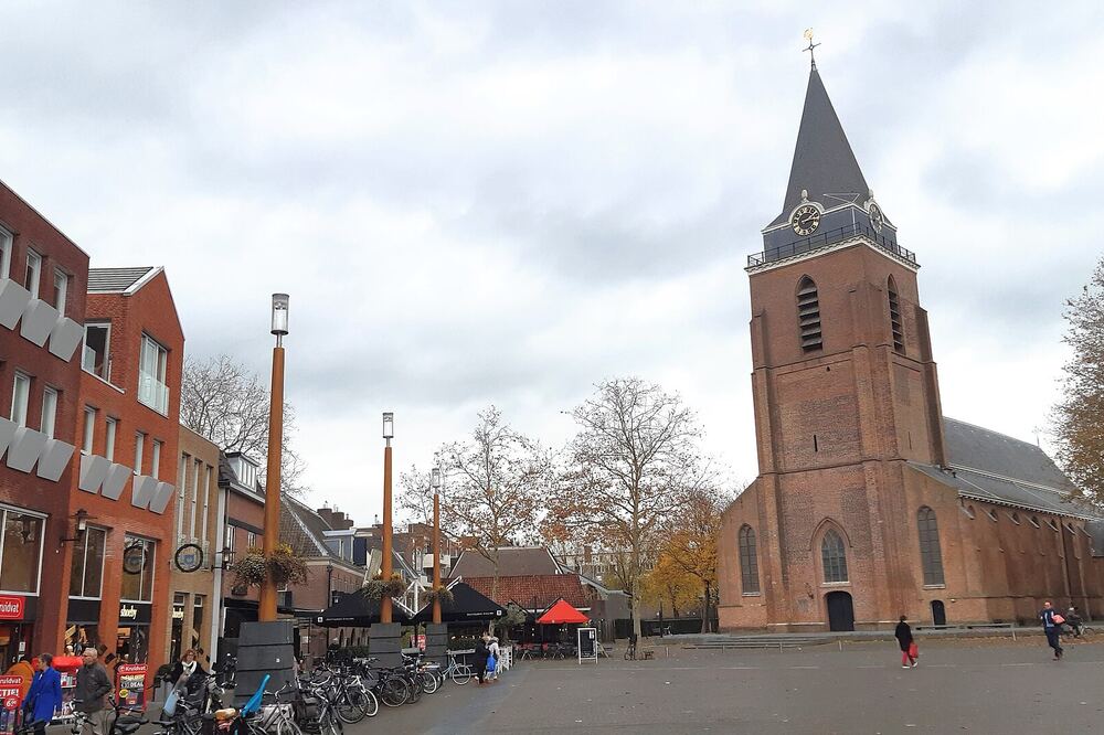De toren van de Petruskerk boven een plein met wandelaars en fietsen in het centrum van Woerden